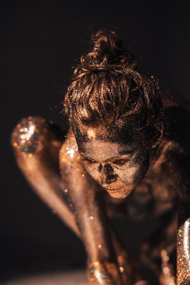 A woman covered in glitter poses artistically against a dark background.